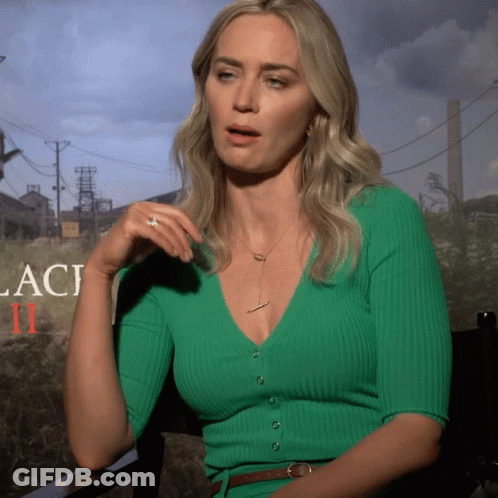 A Woman Wearing A Green Sweater Is Sitting In Front Of A Sign That Says Laci Ii GIF