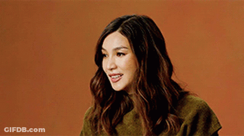 A Woman Wearing A Green Sweater Is Smiling Against An Orange Background . GIF