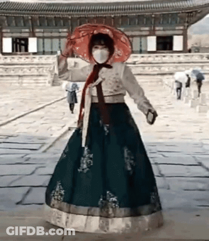 A Woman Wearing A Hanbok Dress And A Mask Is Holding An Umbrella . GIF