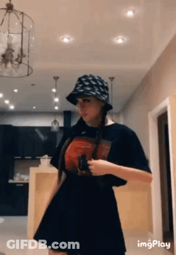 A Woman Wearing A Hat And A Black Skirt Is Standing In A Room . GIF