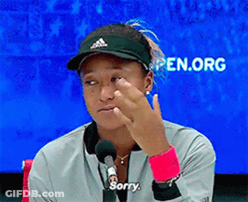 A Woman Wearing A Hat And A Jacket Says Sorry In Front Of A Microphone GIF