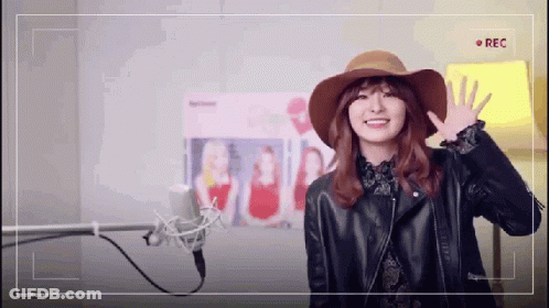 A Woman Wearing A Hat And A Leather Jacket Is Standing In Front Of A Microphone . GIF