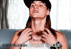 A Woman Wearing A Hat And A Necklace Is Sitting On A Couch . GIF