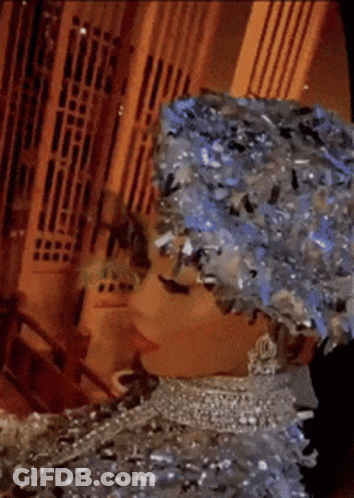 Woman Wearing Hat And Necklace Standing In Front Of Building GIF