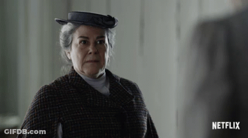 A Woman Wearing A Hat And A Plaid Coat With A Netflix Logo In The Corner GIF