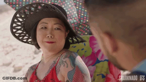 A Woman Wearing A Hat And A Red Bikini Is Sitting On A Beach Chair Looking At A Man . GIF