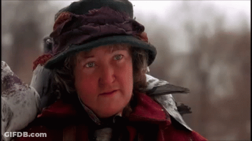 A Woman Wearing A Hat And A Red Coat Is Standing In The Snow GIF