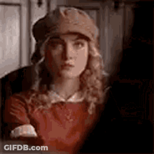 A Woman Wearing A Hat And A Red Shirt Is Looking At The Camera . GIF