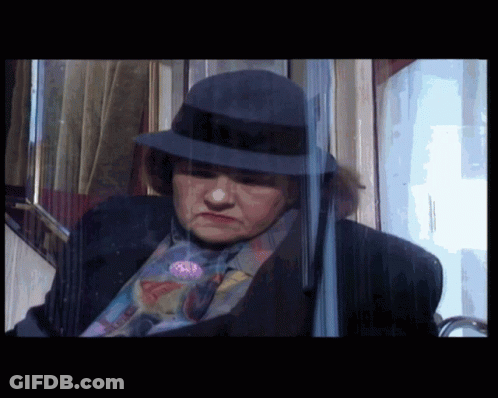 A Woman Wearing A Hat And A Suit Is Behind A Glass GIF
