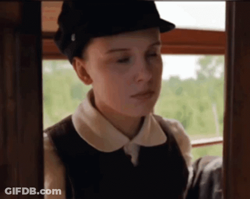 A Woman Wearing A Hat And A Vest Looks Out A Window . GIF