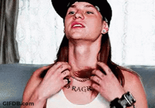A Woman Wearing A Hat And A White Tank Top Has A Tattoo On Her Chest That Says Rage GIF