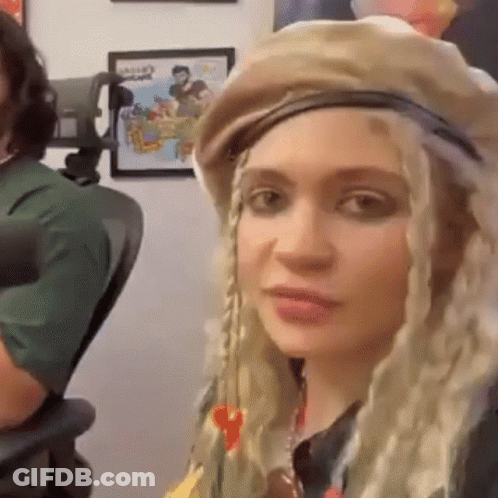 A Woman Wearing A Hat And Braids Is Sitting In A Chair In Front Of A Microphone . GIF