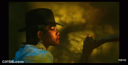 A Woman Wearing A Hat And Earrings Is Smoking A Cigarette In A Vevo Video GIF
