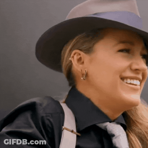 A Woman Wearing A Hat And Earrings Smiles For The Camera GIF
