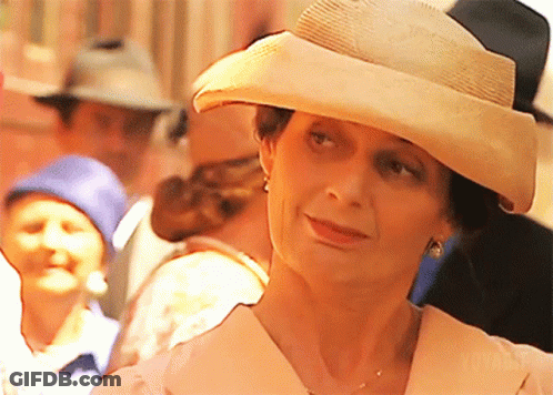 A Woman Wearing A Hat And Earrings Stands In A Crowd Of People GIF