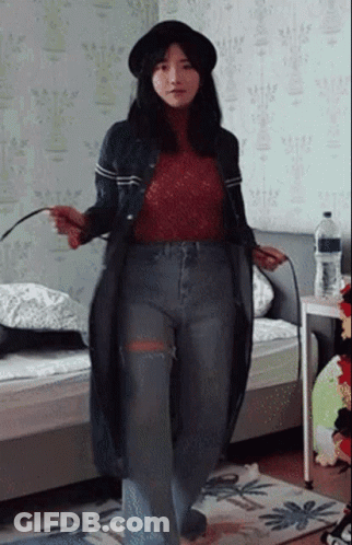 A Woman Wearing A Hat And Jeans Is Standing In A Room GIF