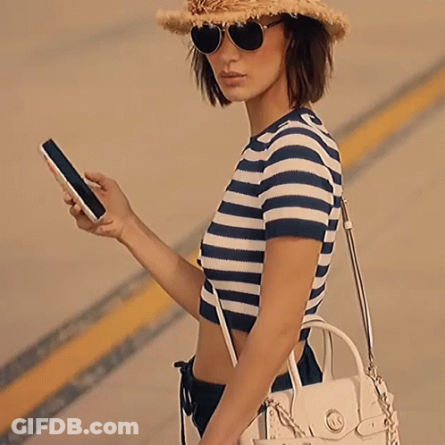 A Woman Wearing A Hat And Sunglasses Is Carrying A White Michael Kors Purse GIF