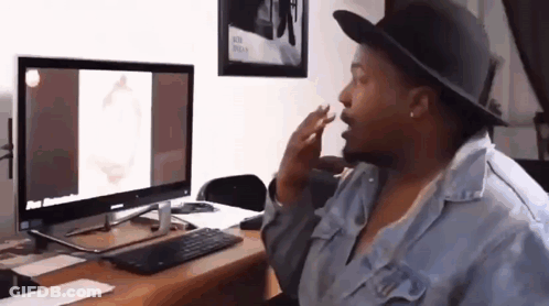 A Woman Wearing A Hat Is Sitting At A Desk In Front Of A Computer Monitor . GIF