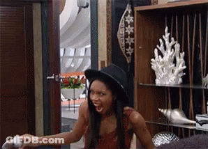 A Woman Wearing A Hat Is Sitting In A Room With A Shelf Full Of Seashells . GIF
