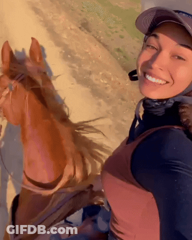 A Woman Wearing A Hat Is Smiling While Riding A Brown Horse GIF