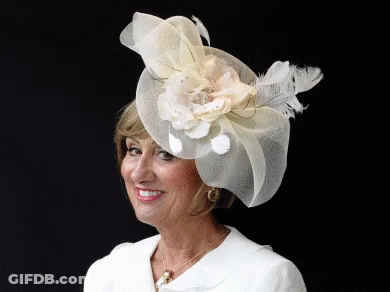 A Woman Wearing A Hat With A Flower And Feathers GIF
