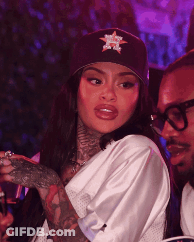 A Woman Wearing A Hat With A Star On It Stands Next To A Man Wearing Glasses GIF