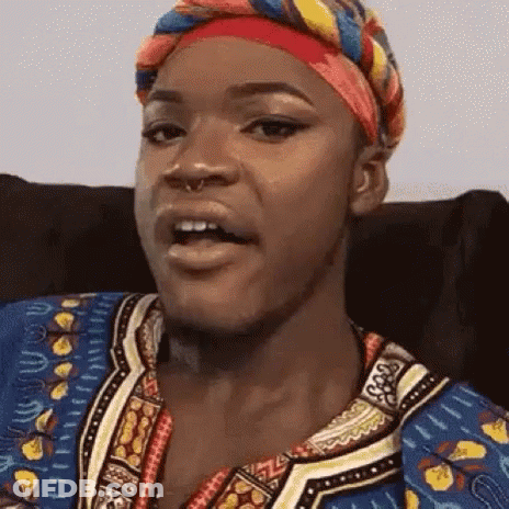 A Woman Wearing A Head Scarf And A Colorful Shirt Is Sitting In A Chair . GIF