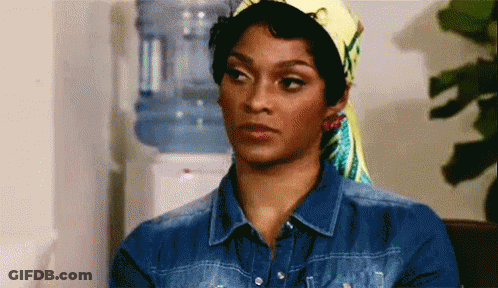 A Woman Wearing A Head Scarf And A Denim Shirt Is Standing In Front Of A Water Cooler . GIF