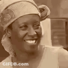 A Woman Wearing A Head Scarf And A Hat Is Smiling . GIF