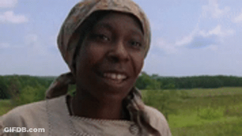 A Woman Wearing A Head Scarf And A Scarf Around Her Head Is Smiling In A Field . GIF