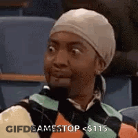 A Woman Wearing A Head Scarf And A Sweater Is Sitting In A Classroom . GIF