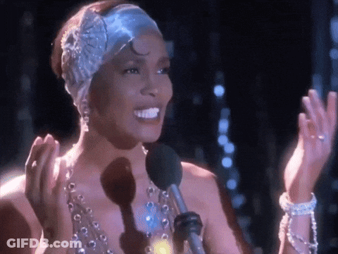 A Woman Wearing A Headband And Pearls Is Singing Into A Microphone . GIF