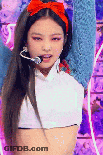 A Woman Wearing A Headband With A Red Bow Is Singing Into A Microphone On A Stage . GIF