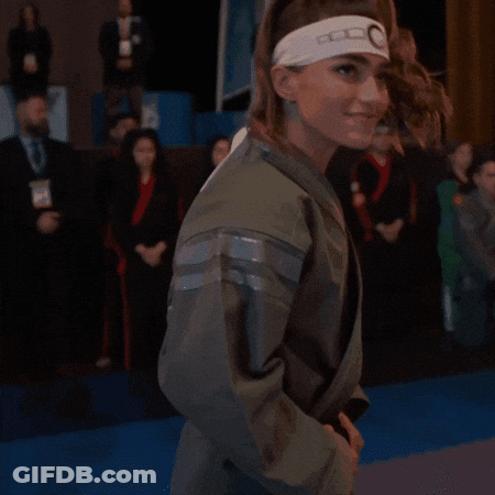 A Woman Wearing A Headband With The Letter G On It Is Covering Her Mouth With Her Hand . GIF