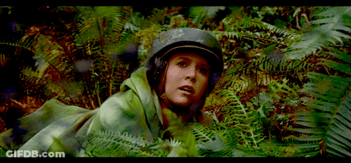 A Woman Wearing A Helmet And A Green Blanket Is Surrounded By Ferns GIF