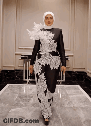A Woman Wearing A Hijab And A Black And White Dress Is Standing In A Hallway GIF