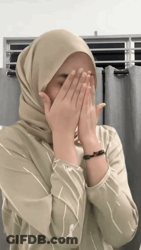 A Woman Wearing A Hijab And A Bracelet Covers Her Face With Her Hands GIF