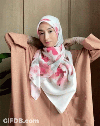 A Woman Wearing A Hijab Is Holding A Pink And White Scarf Around Her Neck GIF