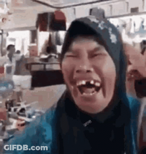 A Woman Wearing A Hijab Is Laughing With Her Mouth Open In A Restaurant . GIF