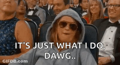 A Woman Wearing A Hoodie And Sunglasses Is Sitting In A Crowd Of People And Making A Funny Face . GIF