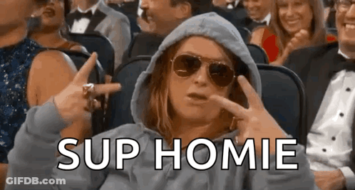 A Woman Wearing A Hoodie And Sunglasses Is Sitting In A Crowd Of People And Making A Funny Face . GIF