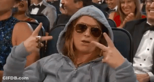 A Woman Wearing A Hoodie And Sunglasses Is Sitting In A Crowd Of People And Making A Peace Sign . GIF
