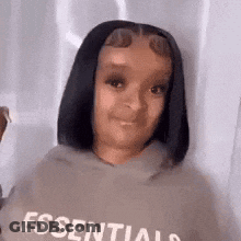 A Woman Wearing A Hoodie With The Word Essentials On It Is Looking At The Camera . GIF