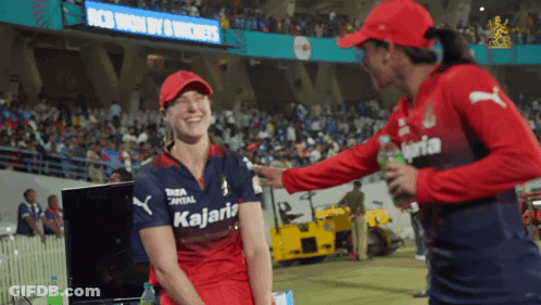 A Woman Wearing A Kalaria Shirt Talks To Another Woman In A Red Hat GIF