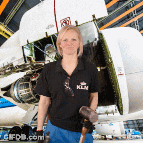 A Woman Wearing A Klm Shirt Holds A Hammer In Front Of An Airplane GIF