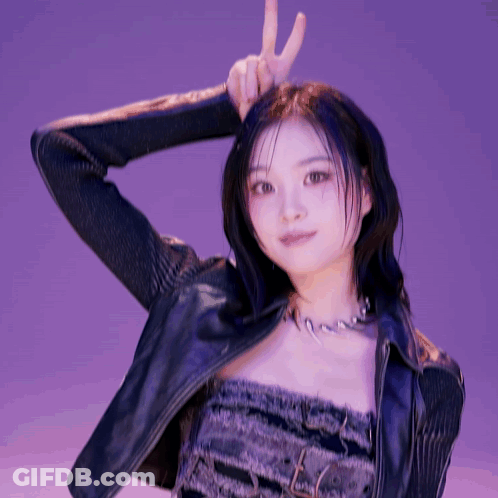 A Woman Wearing A Leather Jacket And A Necklace Is Making A Peace Sign GIF