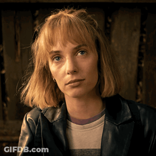 A Woman Wearing A Leather Jacket And A Striped Shirt Looks At The Camera GIF