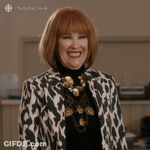 A Woman Wearing A Leopard Print Jacket And A Gold Necklace Smiles For The Camera GIF