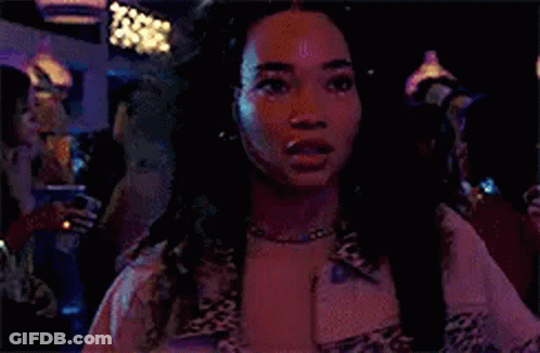 A Woman Wearing A Leopard Print Jacket And A Necklace Is Standing In A Dark Room . GIF