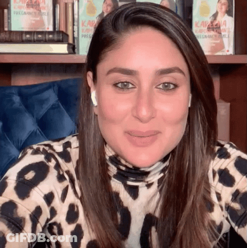 A Woman Wearing A Leopard Print Shirt Is Smiling In Front Of A Bookshelf With Kareena Kapoor Books GIF